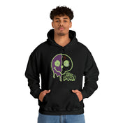 A young man with curly hair is wearing the Stay Spooky Funky Faces Halloween Hoodie (unisex) by Printify. The design features a melting skull in green and purple colors and the text "Stay Spooky." He stands against a plain white background, hands in his hoodie pockets, showcasing his unique artistic expression.