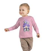 A child is walking and smiling, wearing a light pink "Too Cute To Spook Halloween Toddler Long Sleeve Tee (unisex Tot)" from Printify with an illustration of two owls wearing scarves and the text "Too Cute to Spook." The child has light hair and is also wearing beige pants. This piece of inspirational wear perfectly captures youthful joy against a plain white background.