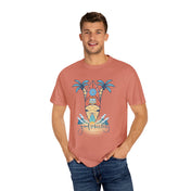 A person stands wearing a Printify Surf's Up! Good Vibes Only Tee (Unisex) with a design featuring an orange and blue surfboard, palm trees, and the text "Good Vibes Only" in the center. The person has hands in their pockets and is smiling. They are also wearing blue jeans, perfectly capturing their artistic expression.