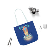 A blue Surf's Up Good Vibes Only Beach Tote by Printify with an illustration of a surfboard, palm trees, and waves reading "Good Vibes Only," lies on a white surface. Surrounding items include an analog camera, wireless earbuds in a case, eyeglasses, and two pens. This setup exudes artistic expression and soulshine.