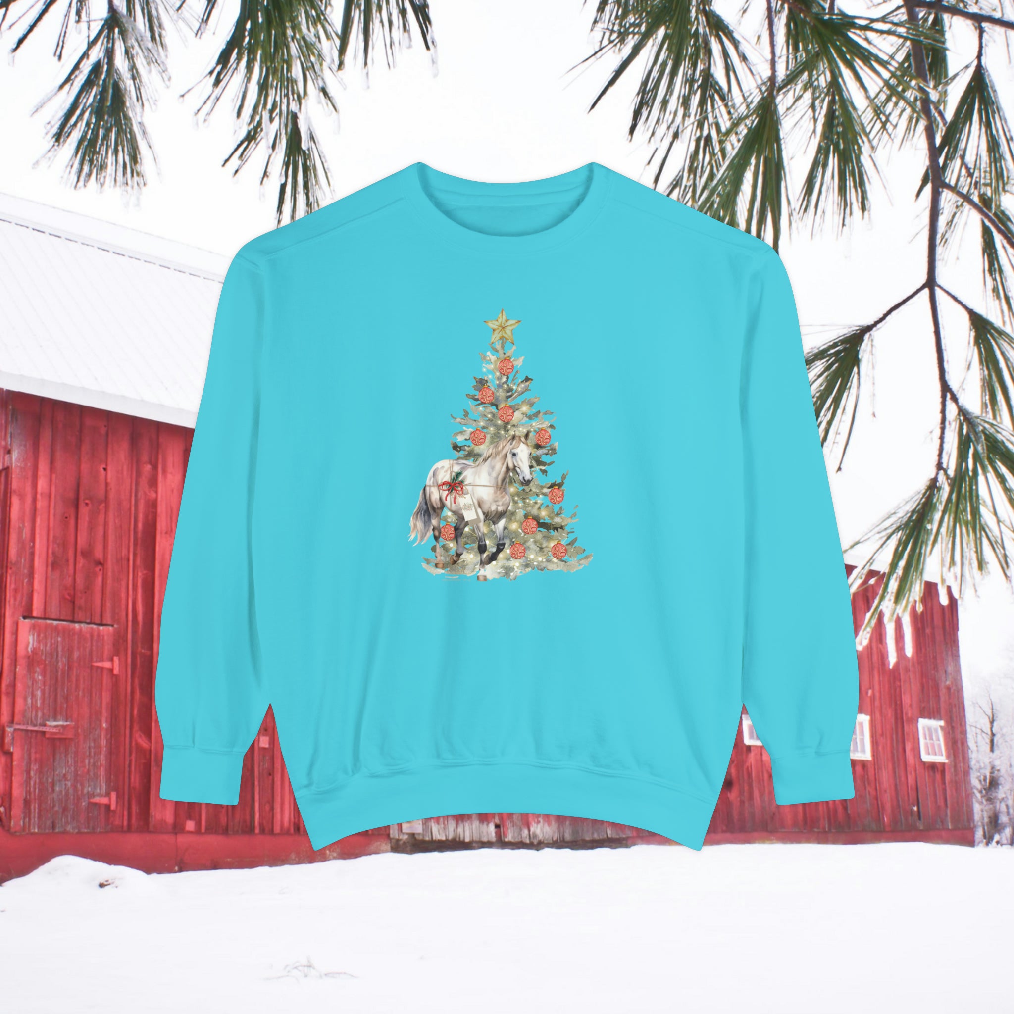 Introducing "The Gift of A Horse Christmas Garment-Dyed Sweatshirt" by Urban SoulShine & co. This unisex sweatshirt, in a calming turquoise shade, showcases a beautifully adorned horse and Christmas tree with ornaments. A red barn is nestled on the snow-covered ground, with pine branches gently hanging above. Designed for a relaxed fit and featuring a garment-dyed finish, this piece blends comfort with festive charm effortlessly.