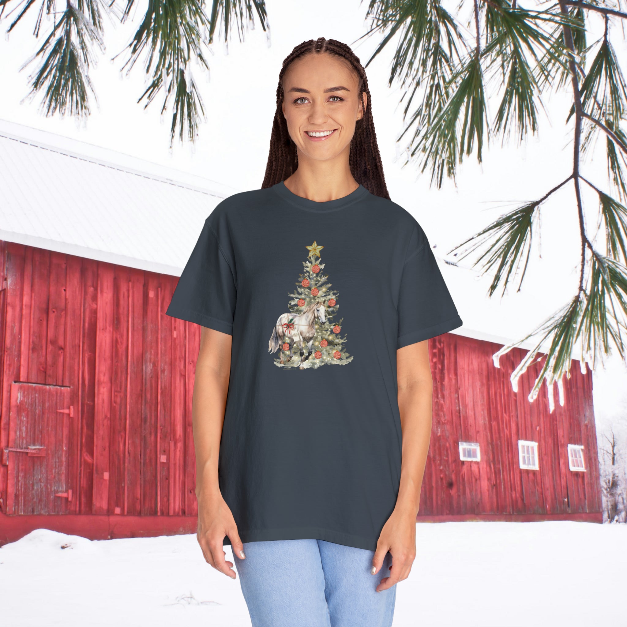 A person wearing "The Gift of A Horse Christmas Garment-Dyed T-shirt" by Urban SoulShine & co stands outside. The snowy backdrop, featuring a red barn and pine branches, perfectly complements the soft feel of the ring-spun cotton material.