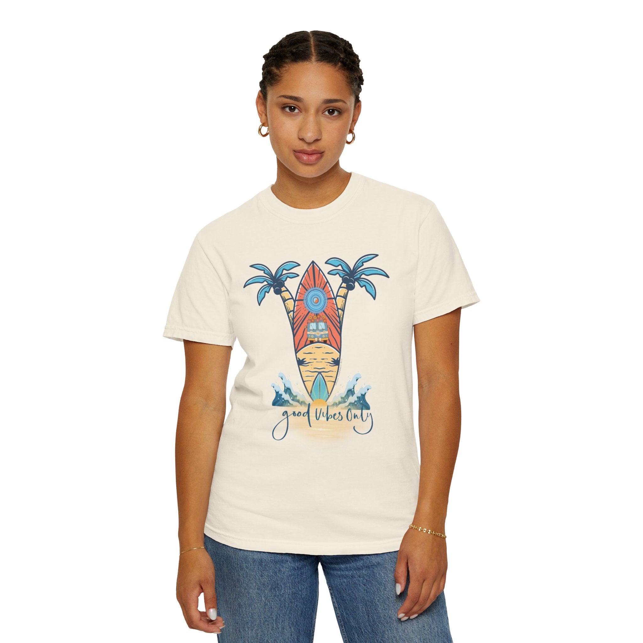 A person stands facing the camera, wearing a white T-shirt featuring a colorful surfboard design with palm trees and ocean waves. The T-shirt has the text "Good Vibes Only" at the bottom, embodying soulshine. The person also wears blue jeans and gold hoop earrings, truly showcasing inspirational wear from Printify’s Surf’s Up! Good Vibes Only Tee (Unisex).