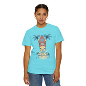 A person with braided hair, wearing a turquoise t-shirt featuring a surfboard, palm trees, and the words "Good Vibes Only," stands against a plain white background. This piece of inspirational wear, the Surf's Up! Good Vibes Only Tee (Unisex) by Printify, is paired with blue jeans and small hoop earrings.