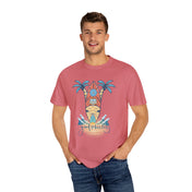 A man is wearing a pink T-shirt featuring a surfing theme with palm trees, a surfboard, and the text "Good Vibes Only" printed on the front. He has his hands in the pockets of his blue jeans and is smiling at the camera, embracing inspirational wear to express himself with the Surf's Up! Good Vibes Only Tee (Unisex) by Printify.