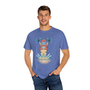 A man wearing a light blue "Surf's Up! Good Vibes Only Tee (Unisex)" by Printify, featuring a design of a surfboard, palm trees, and waves and the text "good vibes only," is smiling with his hands in his pockets. He stands against a plain white background.