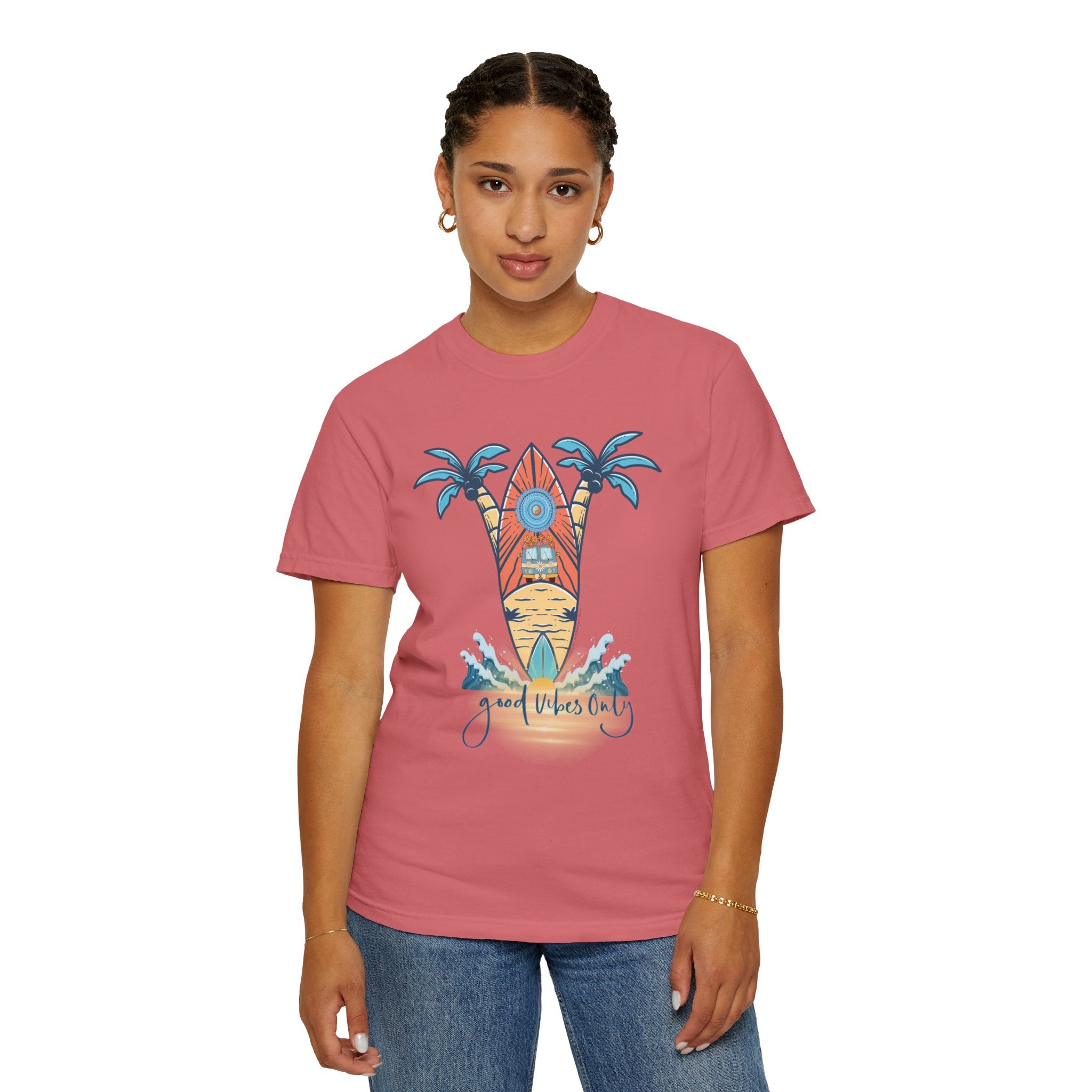 Person stands wearing a pink Surf's Up! Good Vibes Only Tee (Unisex) by Printify with a design of a surfboard, palm trees, and text that reads "Good Vibes Only". The individual has short braided hair, gold hoop earrings, and is also wearing jeans. Their outfit radiates artistic expression and soulshine.