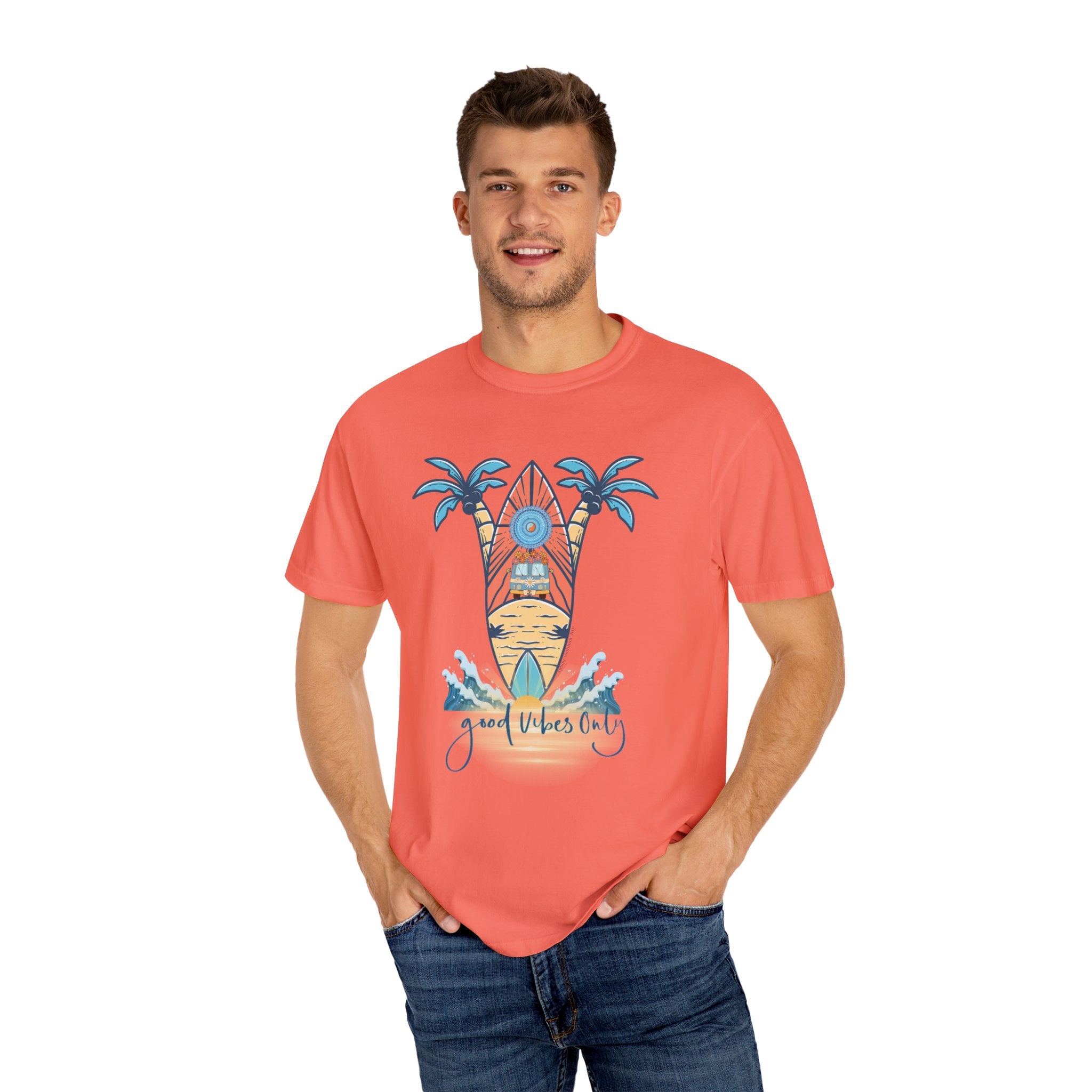 A man is standing and smiling, wearing a coral-colored T-shirt with a beach-themed graphic. The design features a surfboard, palm trees, the sun setting, and the words "Good Vibes Only" written below. Embracing soulshine, he has both hands in his jean pockets while wearing the Surf's Up! Good Vibes Only Tee (Unisex) from Printify.