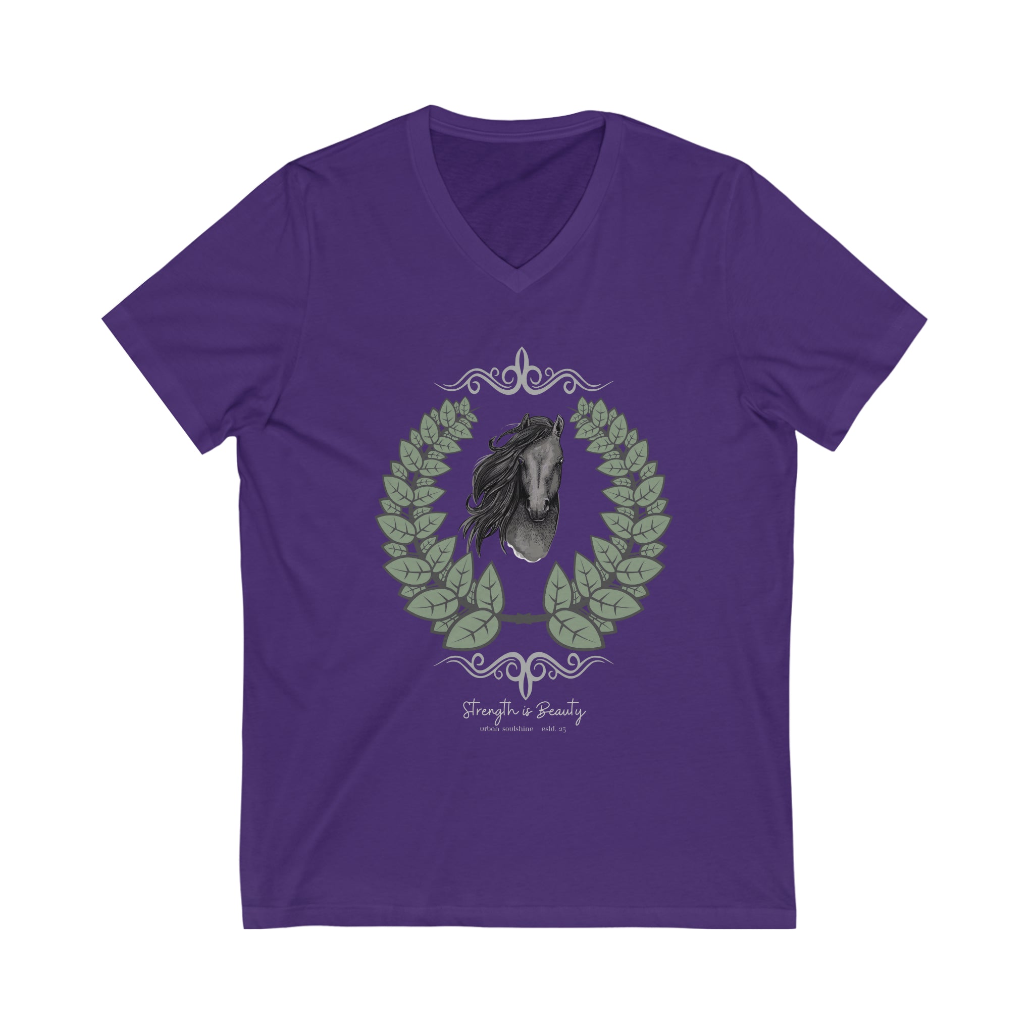 A woman with long hair wearing a gray Urban SoulShine & co Strength is Beauty Horse Tee featuring a horse design is sitting in a partially ruined building. Surrounding the horse image is a leafy wreath. "Strength is Beauty" is written at the bottom in flowing script, daring to inspire. The same horse logo appears on the wall.