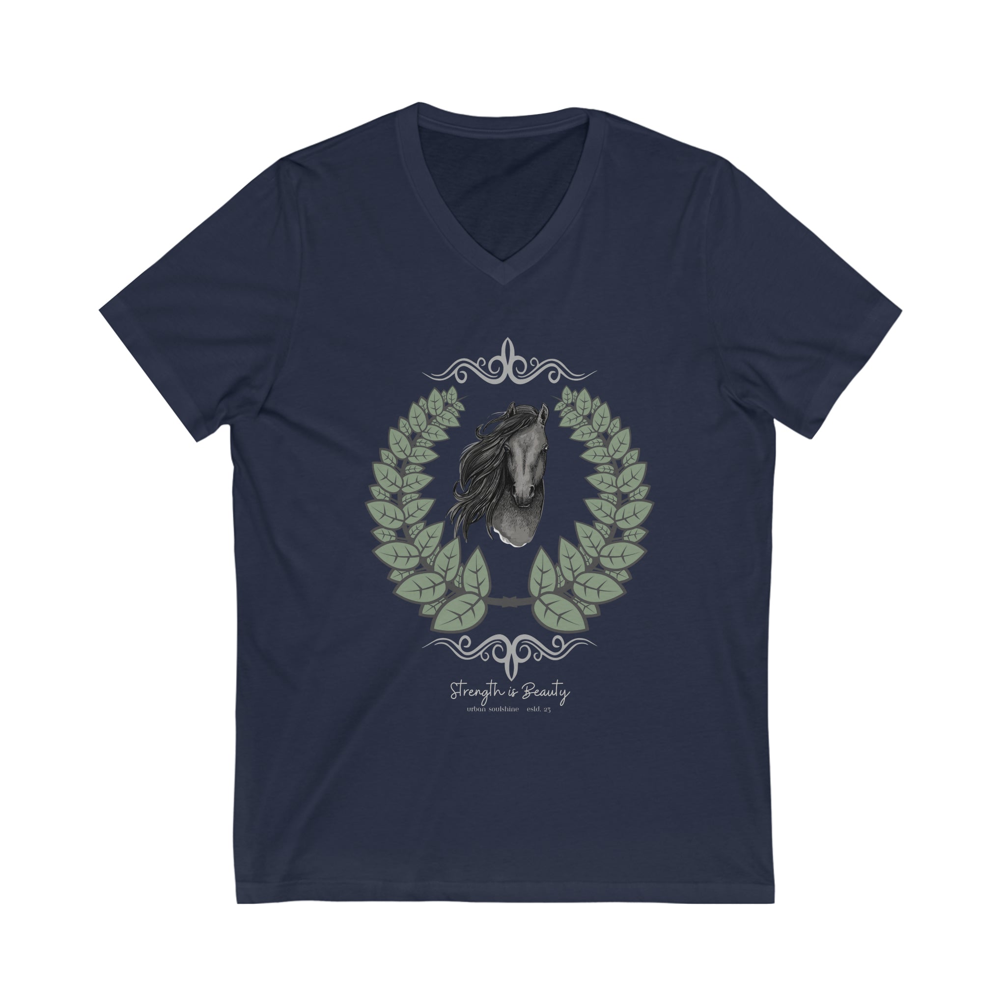 A woman with long hair wearing a gray Urban SoulShine & co Strength is Beauty Horse Tee featuring a horse design is sitting in a partially ruined building. Surrounding the horse image is a leafy wreath. "Strength is Beauty" is written at the bottom in flowing script, daring to inspire. The same horse logo appears on the wall.