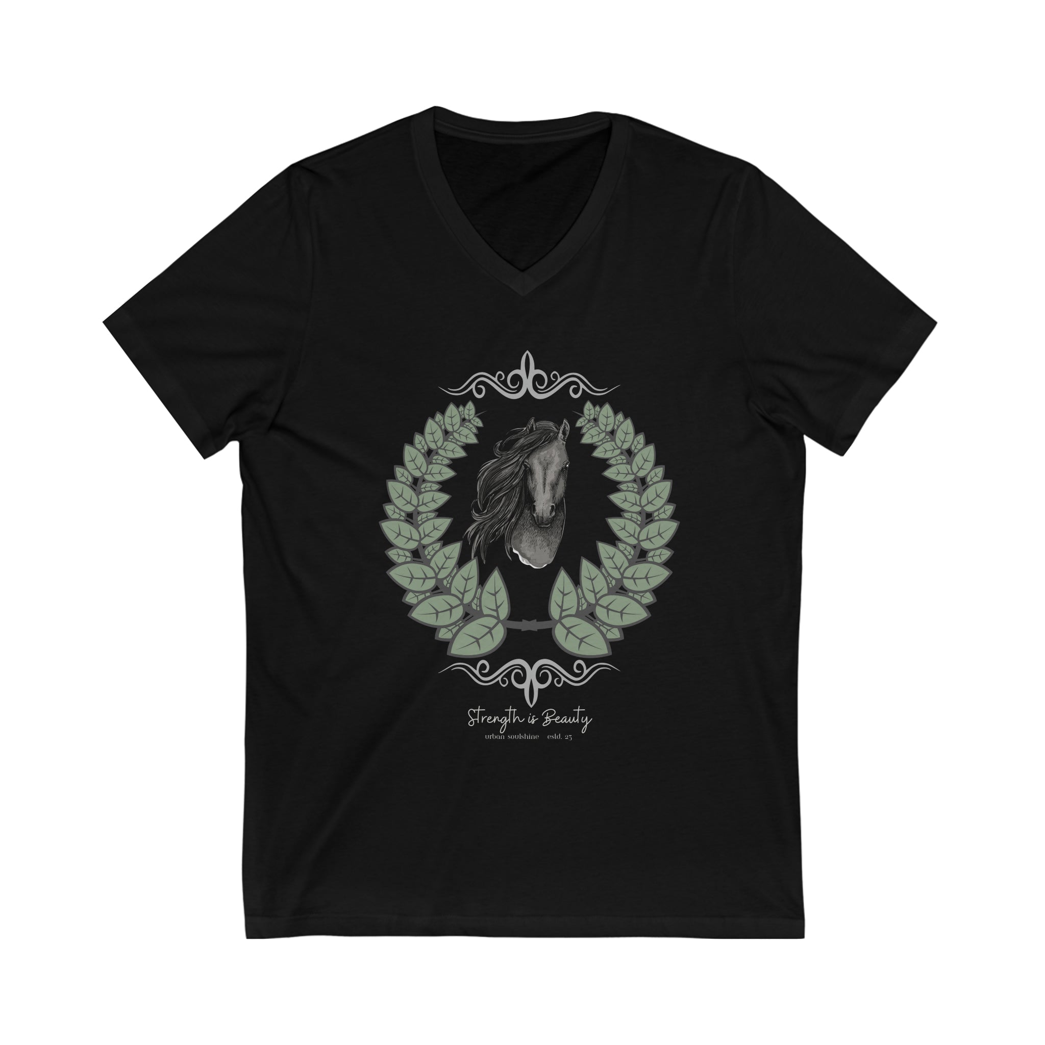 A woman with long hair wearing a gray Urban SoulShine & co Strength is Beauty Horse Tee featuring a horse design is sitting in a partially ruined building. Surrounding the horse image is a leafy wreath. "Strength is Beauty" is written at the bottom in flowing script, daring to inspire. The same horse logo appears on the wall.