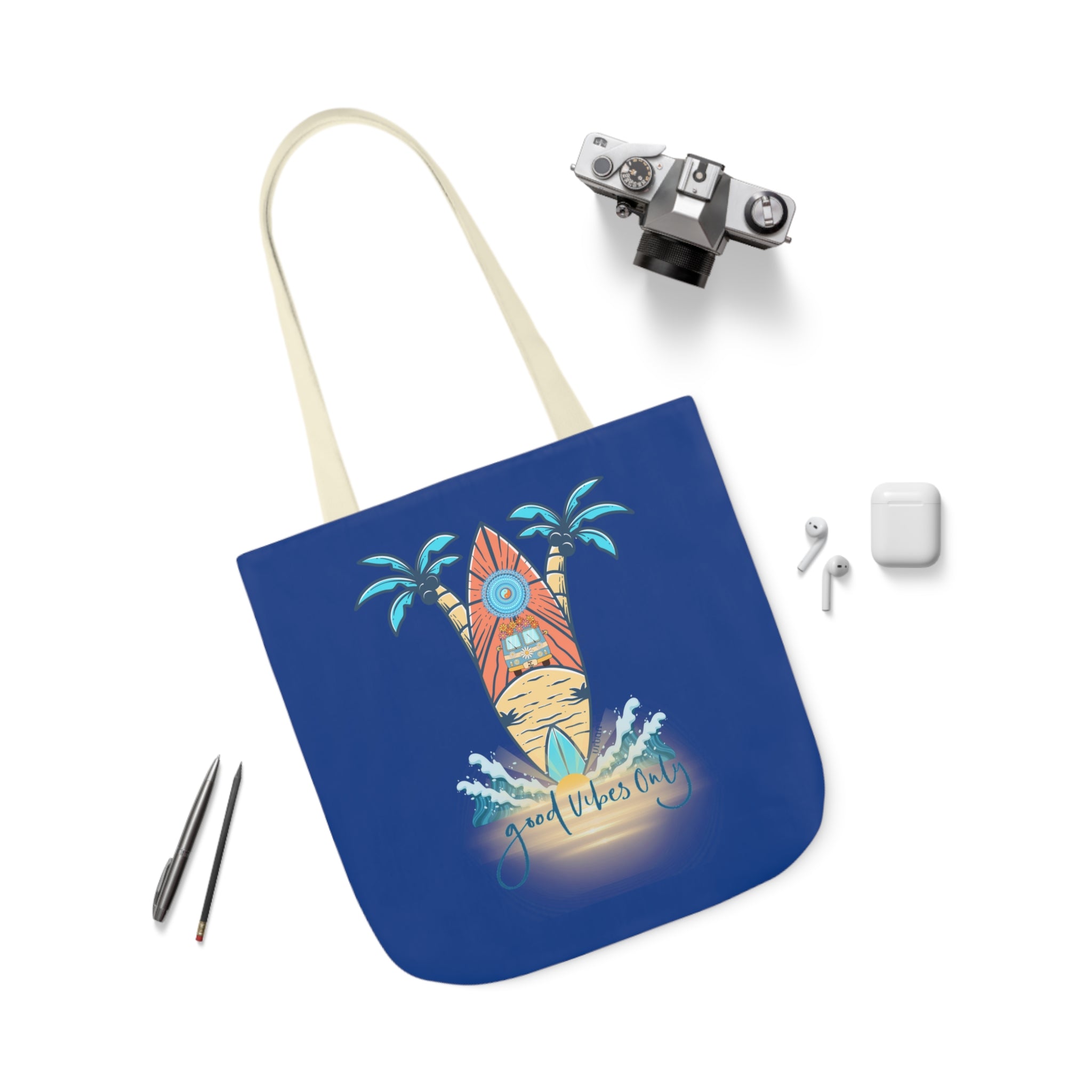 A Surf's Up Good Vibes Only Beach Tote by Printify with "Good Vibes Only" text and a graphic of a surfboard, sun, waves, and palm trees—perfect for those who dare to inspire. Surrounding the bag are a camera, earphones in a case, and two pens.