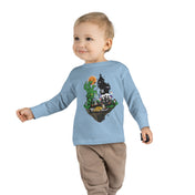 A young child with a slight smile stands against a plain background, wearing a gray long-sleeve shirt and blue jeans. The Spooky Island Halloween Toddler Long Sleeve Tee by Printify features a green, pumpkin-headed figure, a haunted house, and the phrase "Trick or Treat," showcasing an artistic expression perfect for the season.