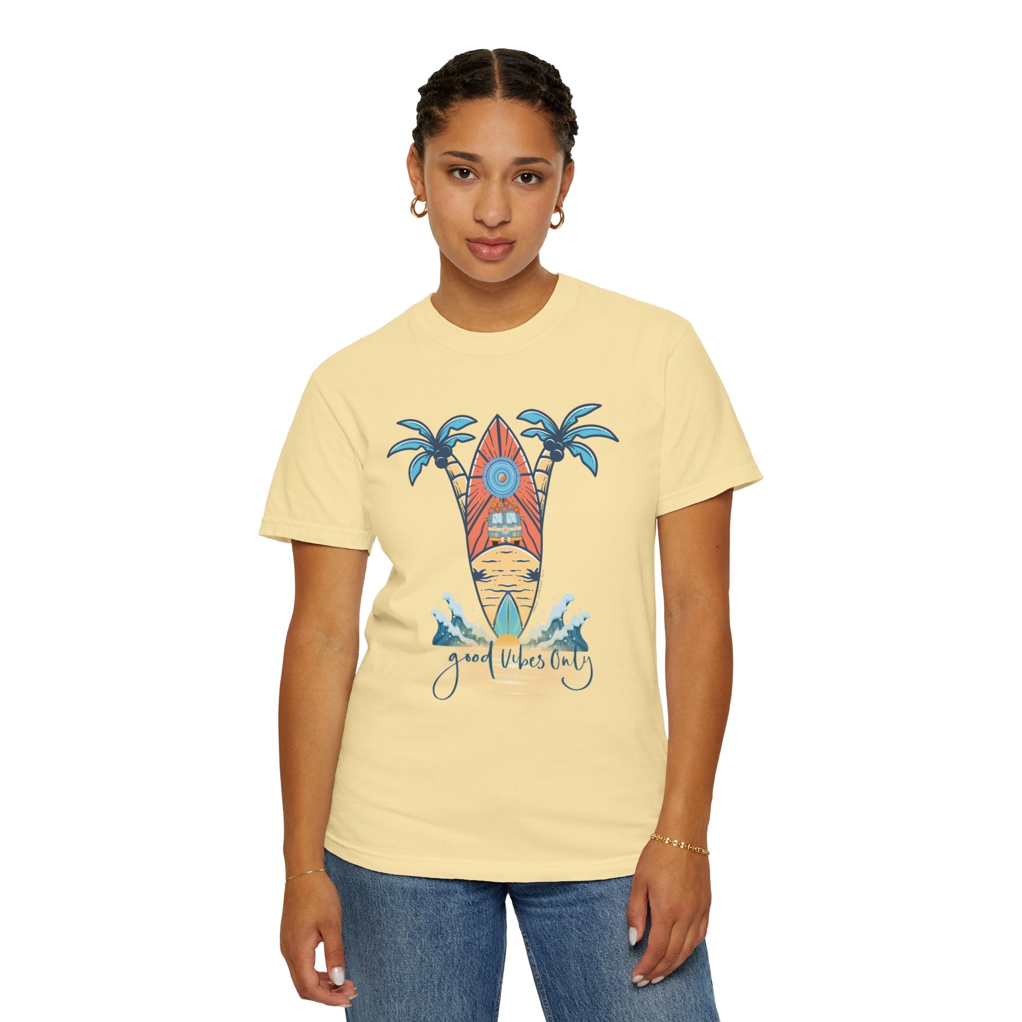 A person with short braided hair is wearing a light yellow Printify Surf's Up! Good Vibes Only Tee (Unisex) featuring a colorful surfboard and palm tree design. The text "Good Vibes Only" is displayed below the illustration, making it perfect for those who love to express themselves. They are also wearing blue jeans and gold hoop earrings.