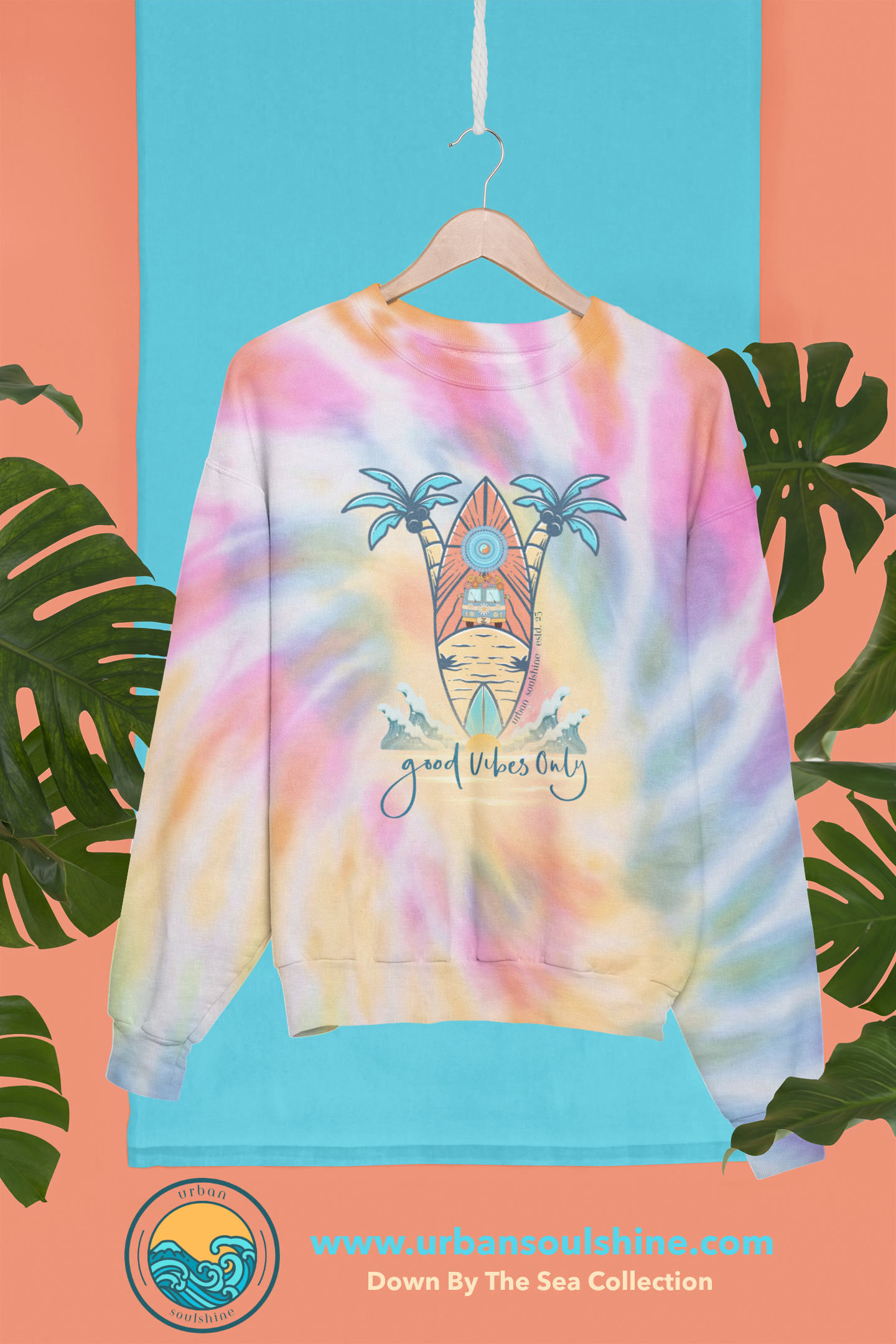 A Surf's Up Good Vibes Only Tie-Dye Sweatshirt (unisex) with the design of a tropical scene, featuring a surfboard, palm trees, and a sun on a beach. The text below the design reads "Good Vibes Only." Made from pre-shrunk PFD cotton, this tie-dye sweatshirt by Urban SoulShine & co is displayed hanging against a blue backdrop with tropical leaves.