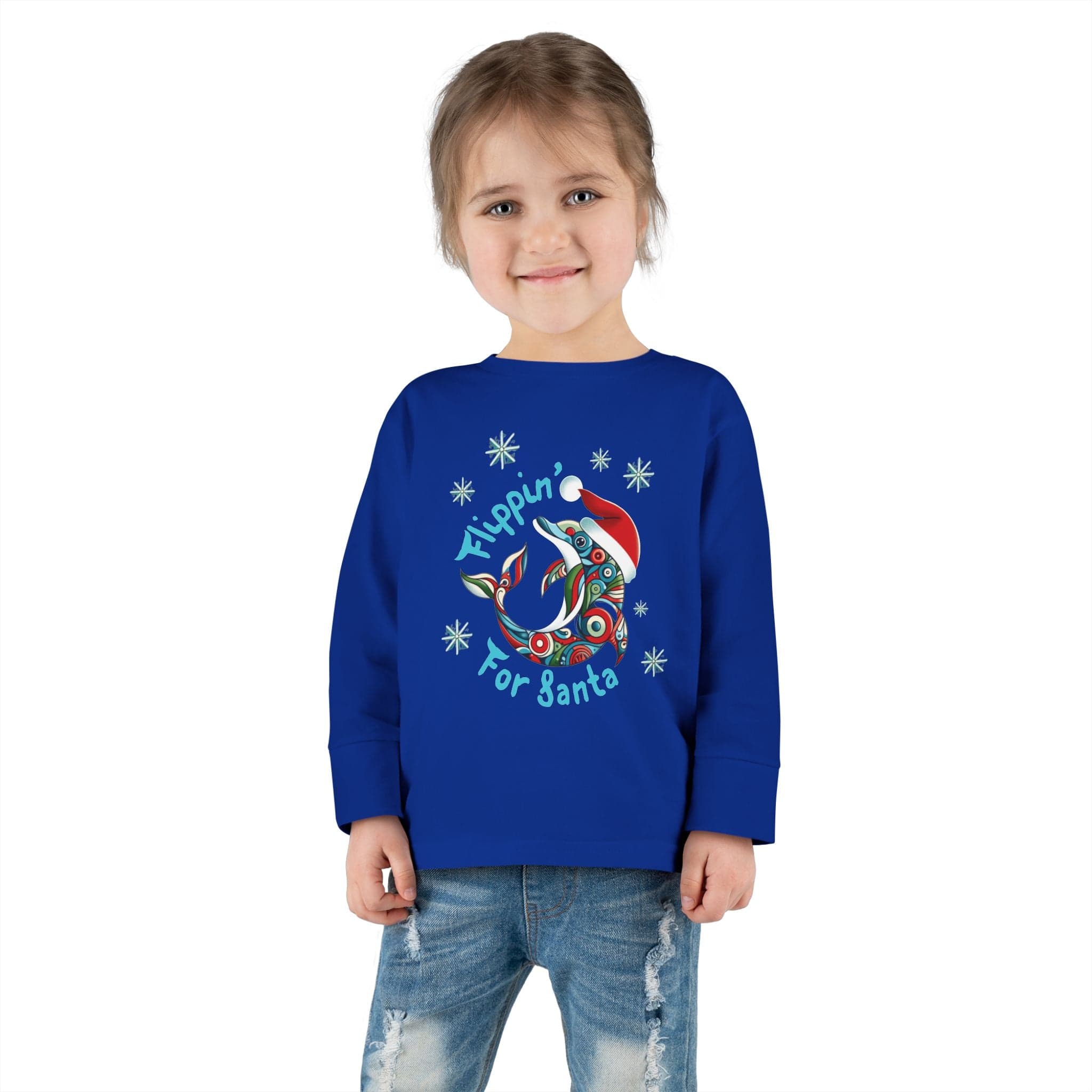 A young child with brown hair beams in a "Flippin' For Santa Christmas Dolphin Long Sleeve Toddler Tee" by Urban SoulShine & Co. Made from 100% cotton, this blue sweatshirt features a cheerful dolphin design and vibrant lettering, pairing beautifully with blue jeans against a simple white background.