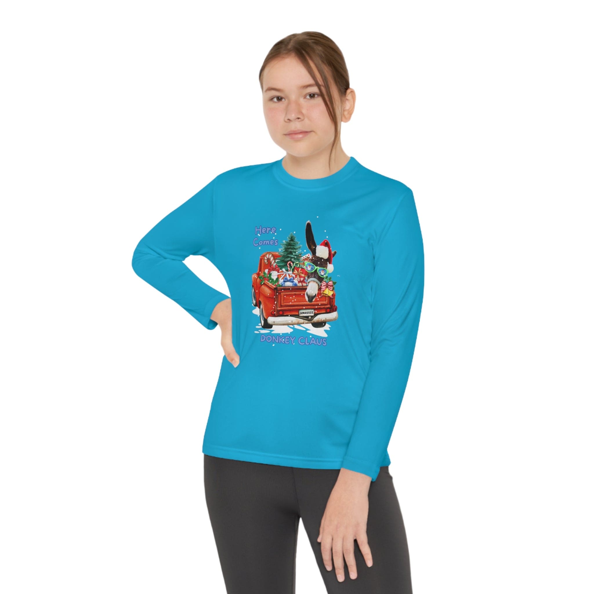 Dressed in a vibrant blue, moisture-wicking polyester long-sleeve shirt with an athletic fit, an individual showcases a festive cartoon featuring a red car loaded with gifts, a Christmas tree, and a rabbit. The Urban SoulShine & Co Here Comes Donkey Claus Long Sleeve Competitor Tee displays the words "Here Comes Dodger Claus." They stand confidently against a white background.