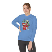 A person wearing the Urban SoulShine & Co YEE HAW Donkey Claus Long Sleeve Competitor Tee (Youth Unisex), featuring an athletic fit and a graphic design of a donkey on a bicycle with a red mailbox, paired with black leggings. The shirt's PosiCharge technology ensures vibrant colors. The plain white background highlights their confident pose as they look at the camera.