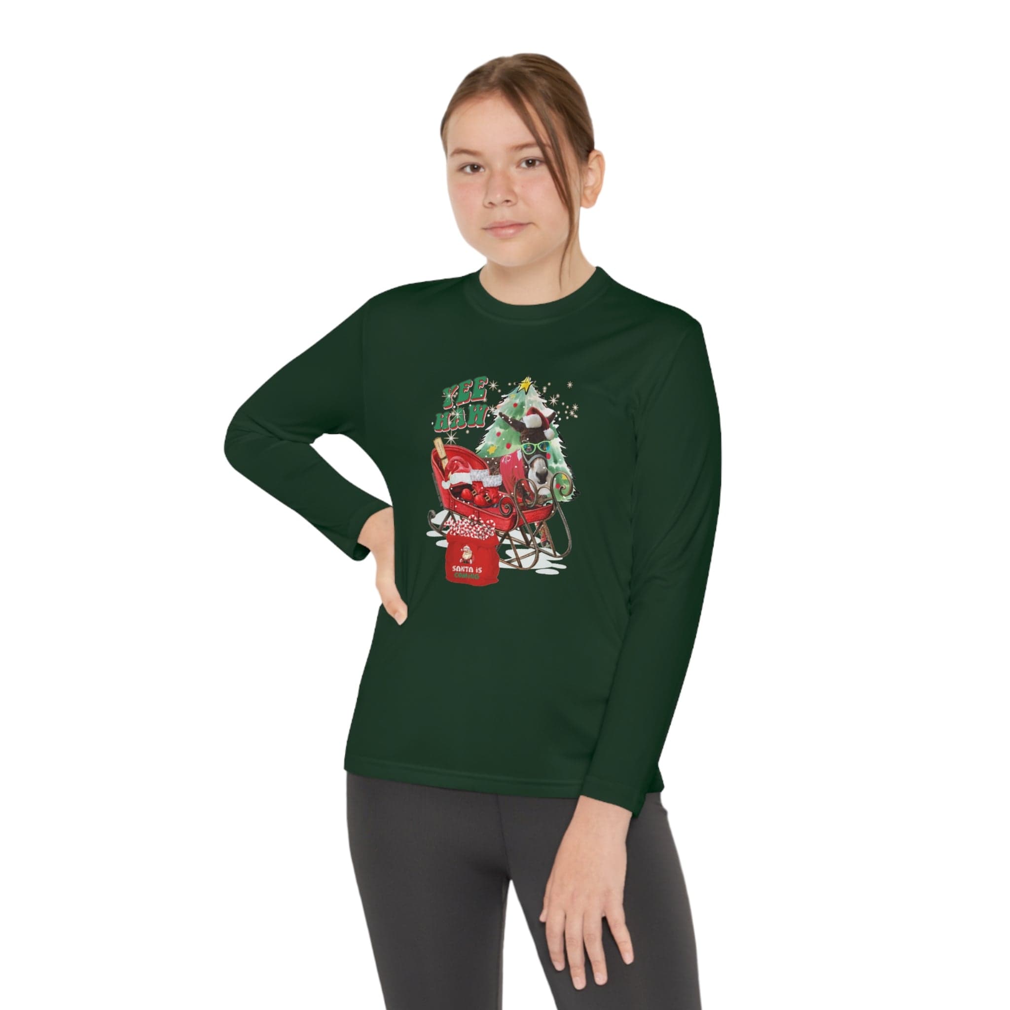 A person is confidently posing with one hand on their hip, wearing the Urban SoulShine & co YEE HAW Donkey Claus Long Sleeve Competitor Tee (Youth Unisex) in dark green. The shirt features an illustrated holiday-themed scene and offers an athletic fit enhanced by PosiCharge technology to maintain vibrant colors, all against a plain white background.