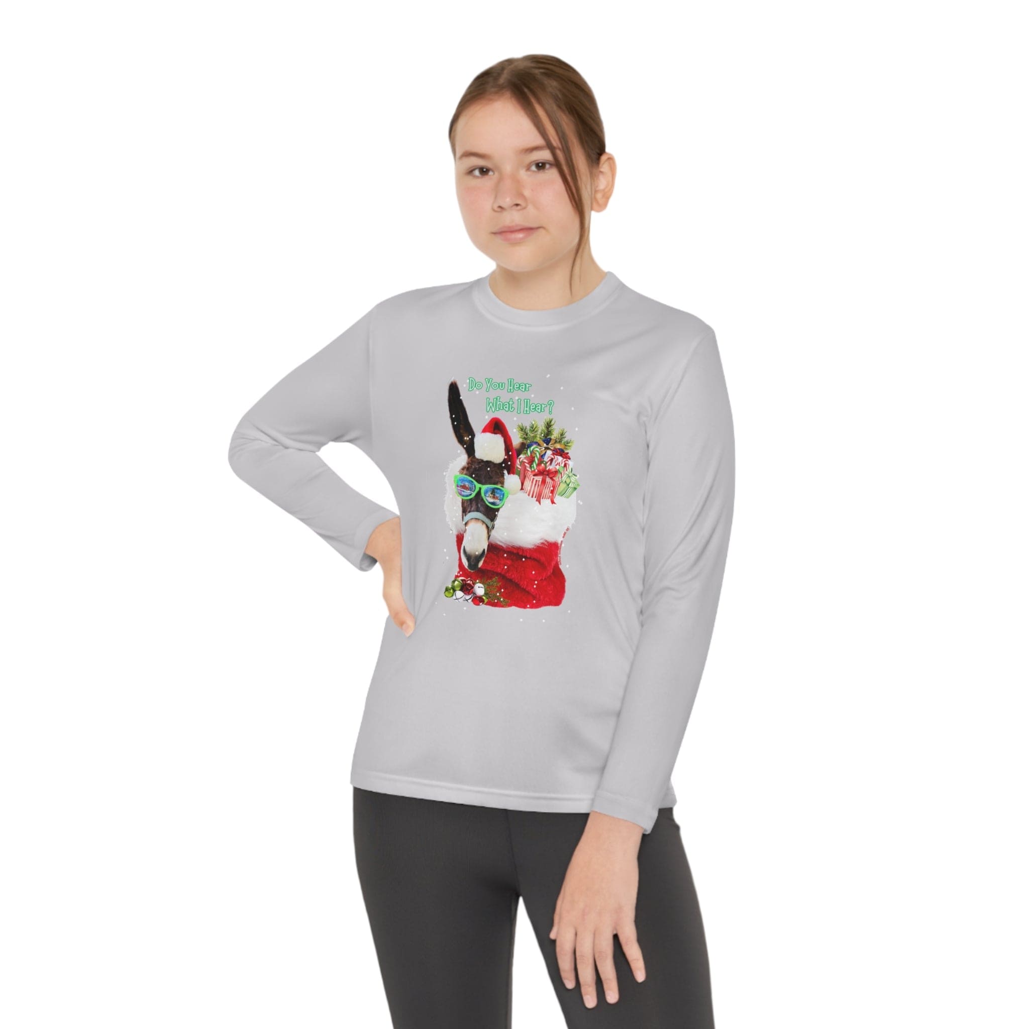 A youth confidently poses against a plain white background, wearing the Urban SoulShine & co's "Do You Hear What I Hear Donkey Claus Long Sleeve Competitor Tee (Youth Unisex)." This gray long-sleeve shirt is adorned with a donkey sporting glasses and a Santa hat, holding gifts and holly.