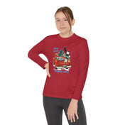 A person wearing a Here Comes Donkey Claus Long Sleeve Competitor Tee (Youth Unisex) by Urban SoulShine & co, featuring an athletic fit, red color, and a festive cartoonish donkey dressed as Santa in a red car graphic, poses confidently with one hand on their hip. The moisture-wicking polyester design pairs perfectly with their black pants.