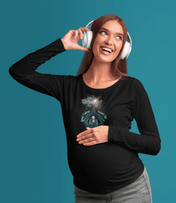 A woman wearing headphones smiles while touching her pregnant belly, adorned in a Good Tidings Great Joy Christmas Wish Glowing Long Sleeve Tee from Urban SoulShine & Co. The solid teal background highlights the artistic light projection design on her shirt, adding a modern touch to the serene moment.