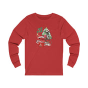 The YEE HAW Santa Is Coming Donkey Claus Long Sleeve Tee by Urban SoulShine & co is a unisex red jersey shirt that showcases a festive cartoon Christmas scene. It features a green monster decorating a tree alongside a sleigh brimming with presents, capturing the charm of the holiday season. The text reads "YEE HAW.