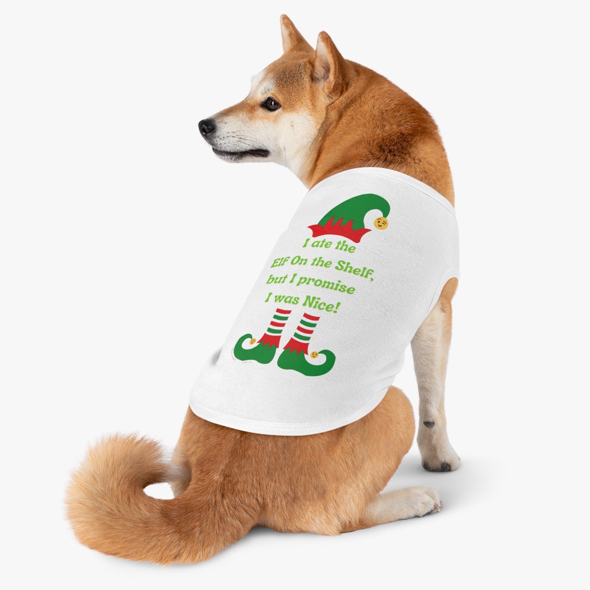 A Shiba Inu, wearing the Urban SoulShine & co "I Ate the Elf On the Shelf Holiday Pet Shirt," sits with its back turned. This white shirt features a festive design with elf legs and the cheerful message: "I ate the ELF on the Shelf, but I promise I was Nice!" displayed in vibrant red and green letters. Additionally, it is machine washable!