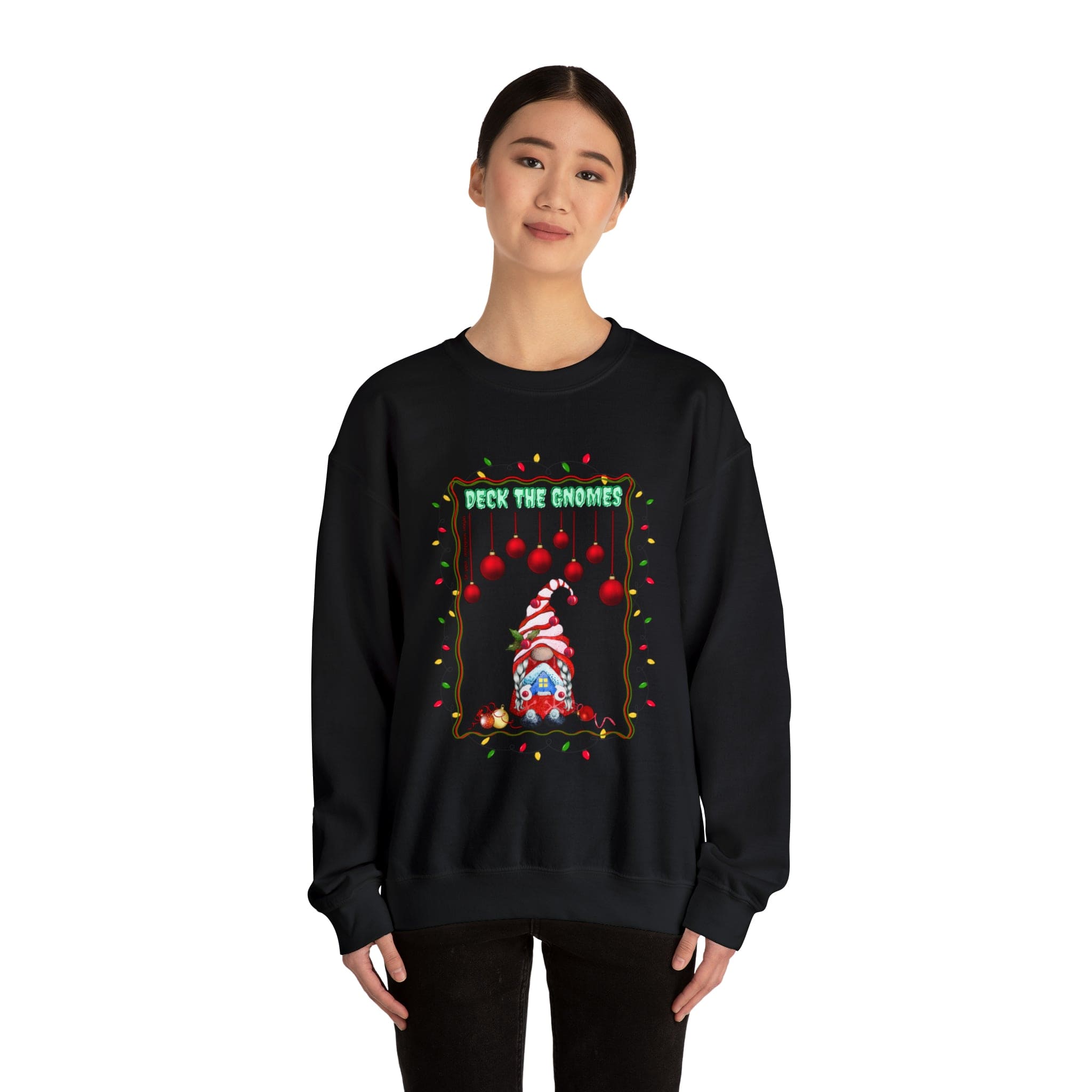 An individual is dressed in the Urban SoulShine & co Deck The Gnomes Holiday Crewneck Sweatshirt, a unisex garment made from a comfortable polyester cotton blend. The sweatshirt is adorned with a festive gnome graphic and the phrase "Deck the Gnomes," complemented by cheerful lights and ornaments on a simple white background.