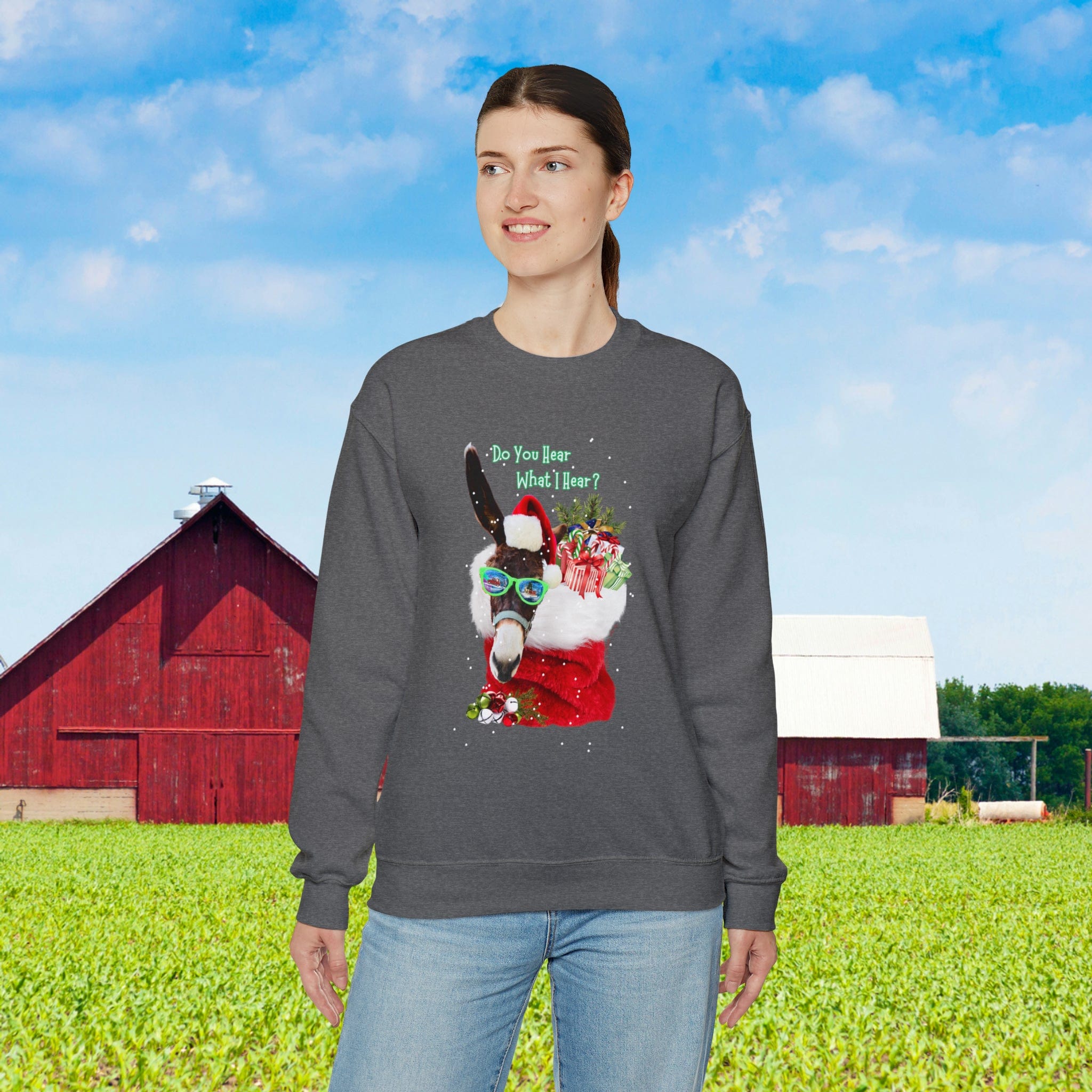 In a field, someone is wearing the Urban SoulShine & co Do You Hear What I Hear Donkey Claus Christmas Sweatshirt (Unisex), which features a festive illustration of a llama. The sweatshirt showcases the text "Do you hear what I hear?" with a scenic background of a red barn and blue sky.