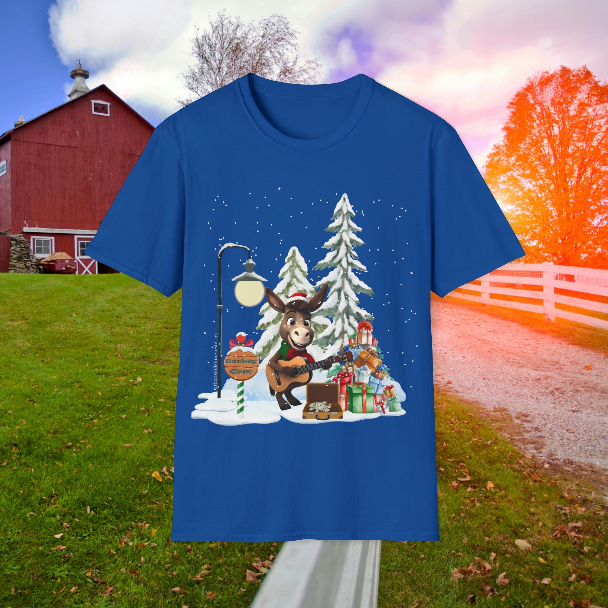 The Donkey Claus Street Singer Holiday Soft Tee (Unisex) by Urban SoulShine & co features a blue design that beautifully depicts a festive scene. It highlights a donkey named Donkey Claus, playing guitar amid snow-dusted trees and presents under a sunset sky. The backdrop includes a red barn and white fence, all crafted on 100% cotton fabric to capture the spirit of Christmas cheer.